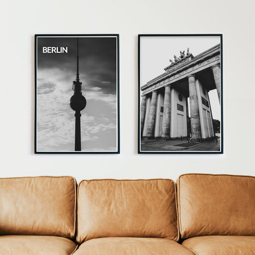 2er Berlin Poster Set in schwarz weiß vom Fernsehturm und dem Brandenburger Tor. Bilder in schwarzen Bilderrahmen über einem braunen Sofa.