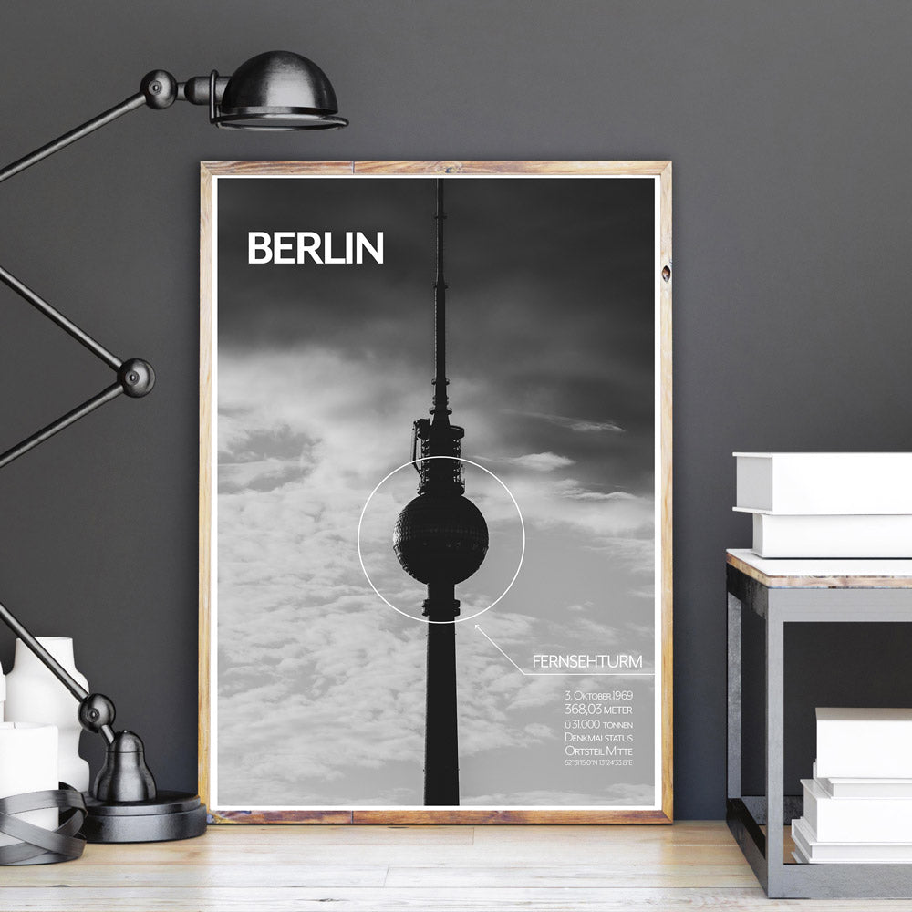 Schwarz Weiß Berlin Poster vom Fernsehturm mit Fakten vom Turm unten rechts. Berlin Schriftzug oben links. Bild im Holzrahmen an einer grauen Wand.