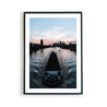 Frankfurt am Main Poster. Boot fährt über den Main, im Hintergrund die Frankfurter Skyline zum Sonnenuntergang. Bild mit weißen umlaufenden Rand. Gerahmt im schwarzen Rahmen.