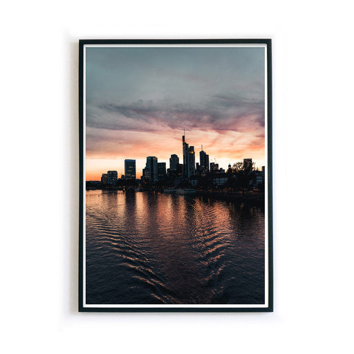Frankfurt Skyline Poster zum Sonnenuntergang. Kraftvoller Himmel mit Spiegelungen im Main. Bild im schwarzen Bilderrahmen.