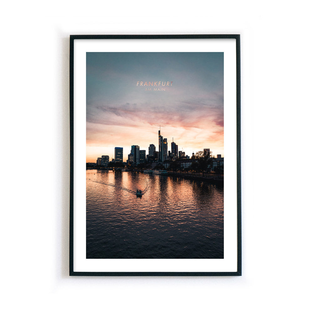 Frankfurt am Main Skyline Poster. Farbenfroher Sonnenuntergang, kleines Boot fährt im Vordergrund über den Main. Bild mit weißen umlaufenden Rand. Gerahmt im schwarzen Rahmen.