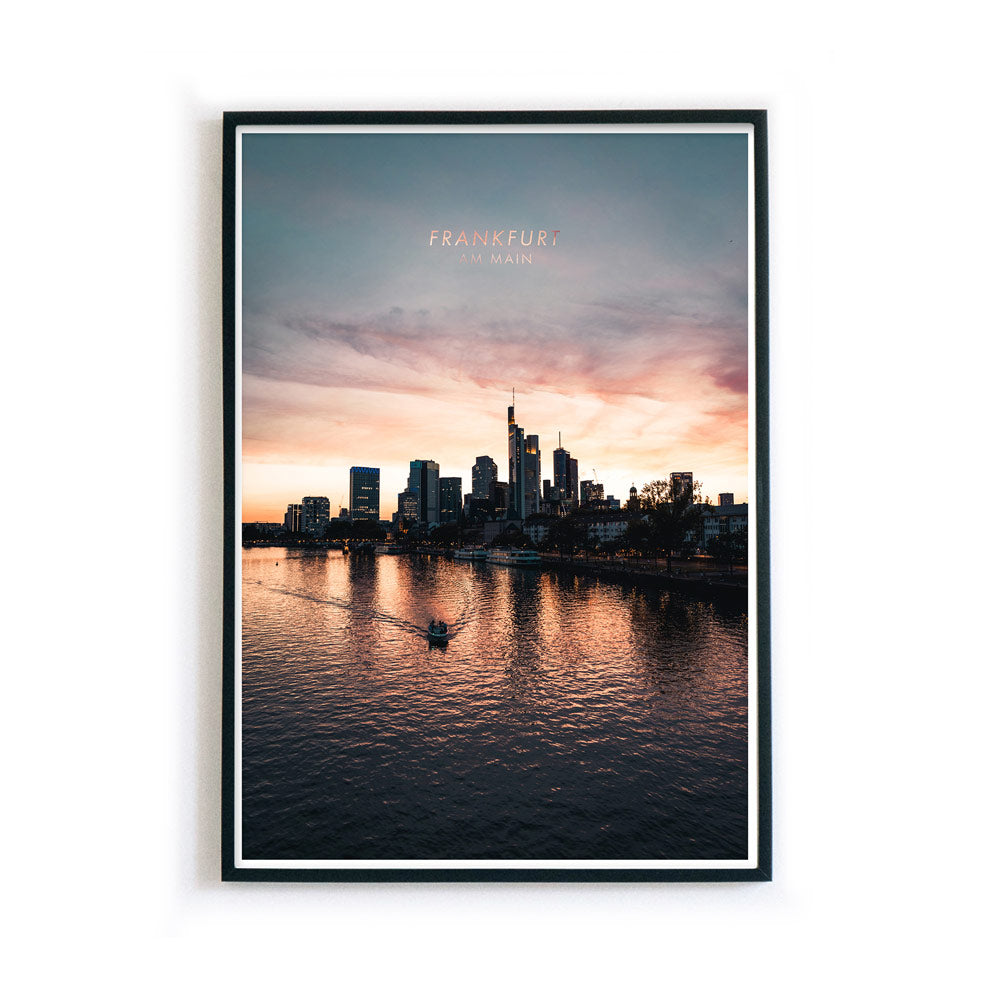 Frankfurt am Main Skyline Poster. Farbenfroher Sonnenuntergang, kleines Boot fährt im Vordergrund über den Main. Bild im schwarzen Rahmen.