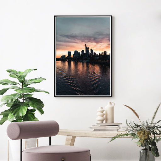 Frankfurt Skyline Poster zum Sonnenuntergang. Kraftvoller Himmel mit Spiegelungen im Main. Bild im schwarzen Rahmen an der Wand über einem Tisch.