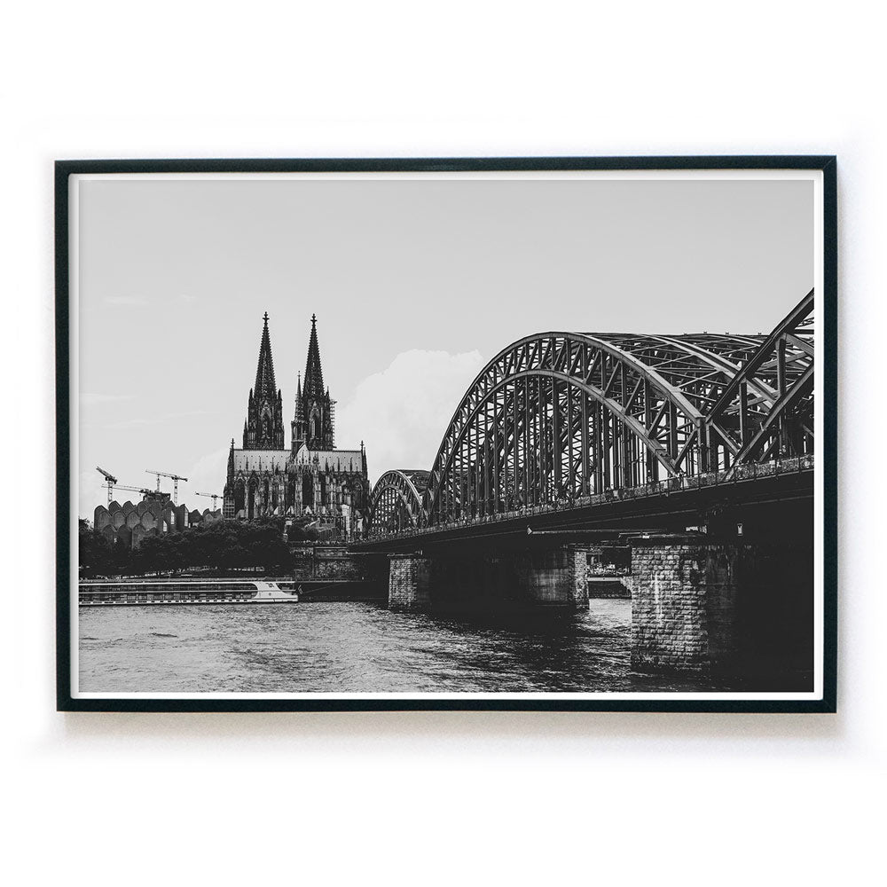 Schwarz Weiß Köln Poster im Querformat, gerahmt in einem schwarzen Bilderrahmen. Bild der Hohenzollernbrücke, dem Rhein und dem Kölner Dom.