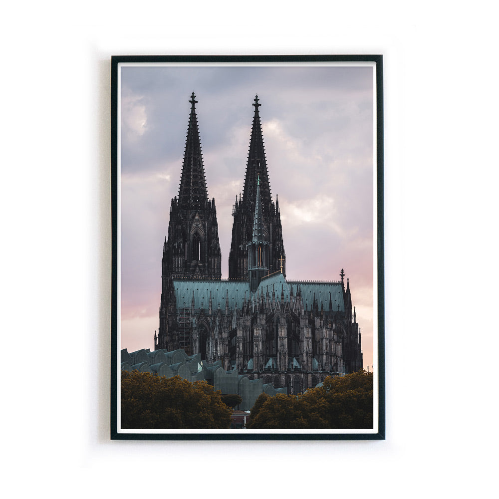 Kölner Dom Poster im Sonnenuntergang mit rötlichem Himmel. Im Vordergrund das Museum Ludwig und Bäume. Wandbild ist gerahmt.