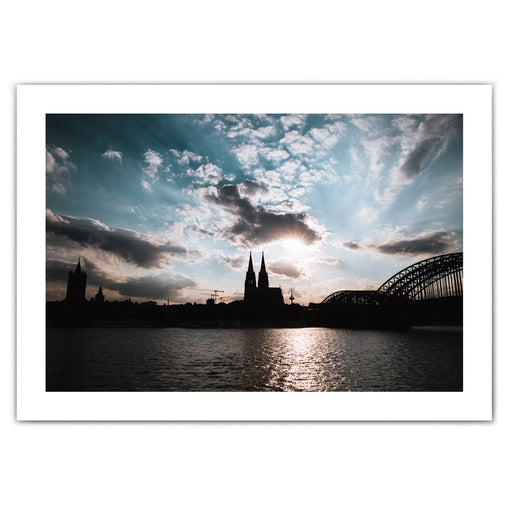 Köln Skyline Poster im Querformat. Sonnenuntergang über dem Kölner Dom bei leicht bewölkten blauen Himmel. Bild mit weißen Rand.