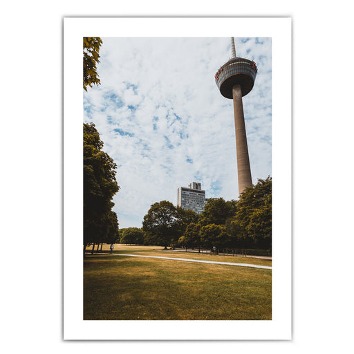 Retro Köln Poster vom Fernsehturm im grünen Gürtel. Grüne Wiese und Bäume im Vordergrund bei blauem bewölkten Himmel. Bild mit weißen umlaufenden Rand.