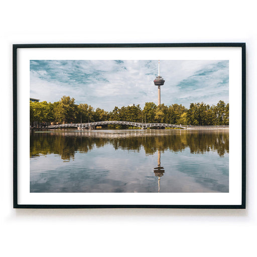 Köln Bild im Bilderrahmen als Querformat. Motiv ist der Fernsehturm, eine Brücke und Bäume, die sich im See spiegeln. Bild mit weißen Rand.