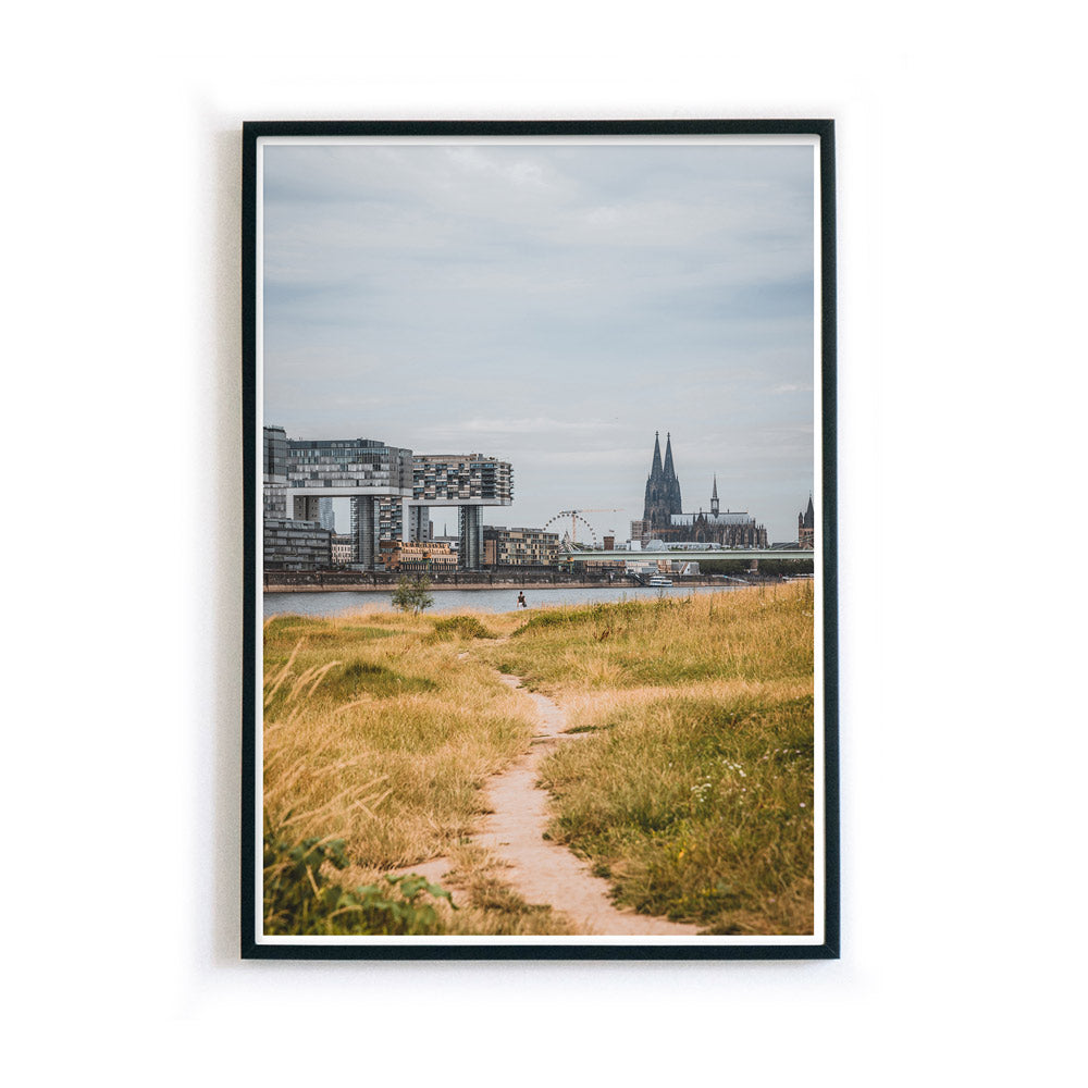 Köln Poster mit Bilderrahmen von einem Weg der Richtung Köln führt. Der Rhein, Kölner Dom und Kranhäuser im Hintergrund vom Bild.